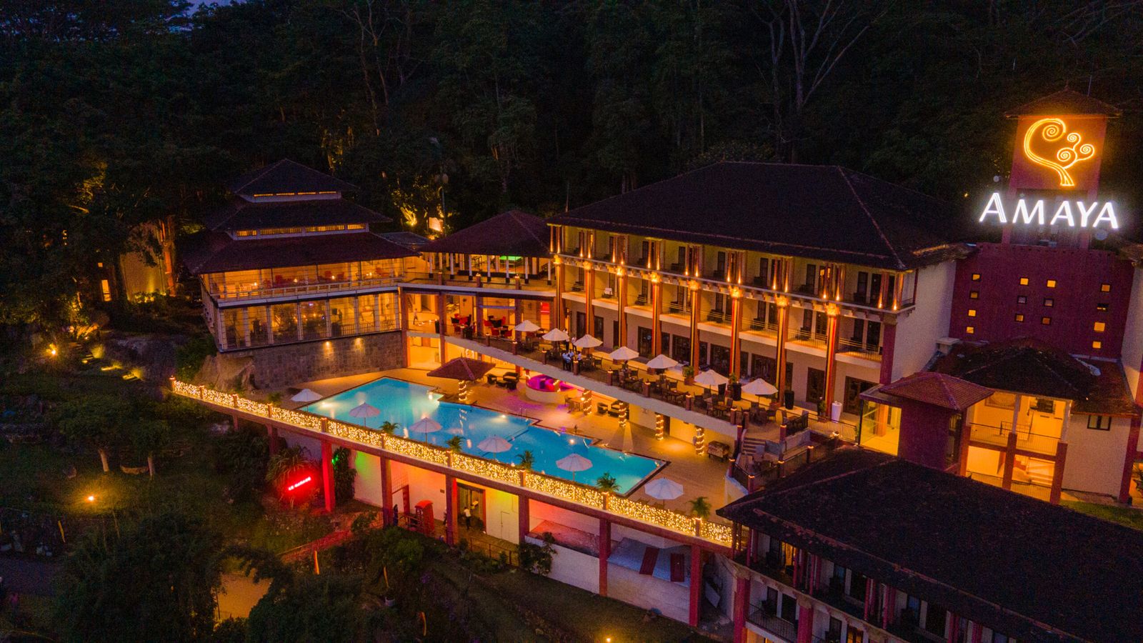The hotel lit up at night around its pool, seen from above, with the resort's sign on a tower.
