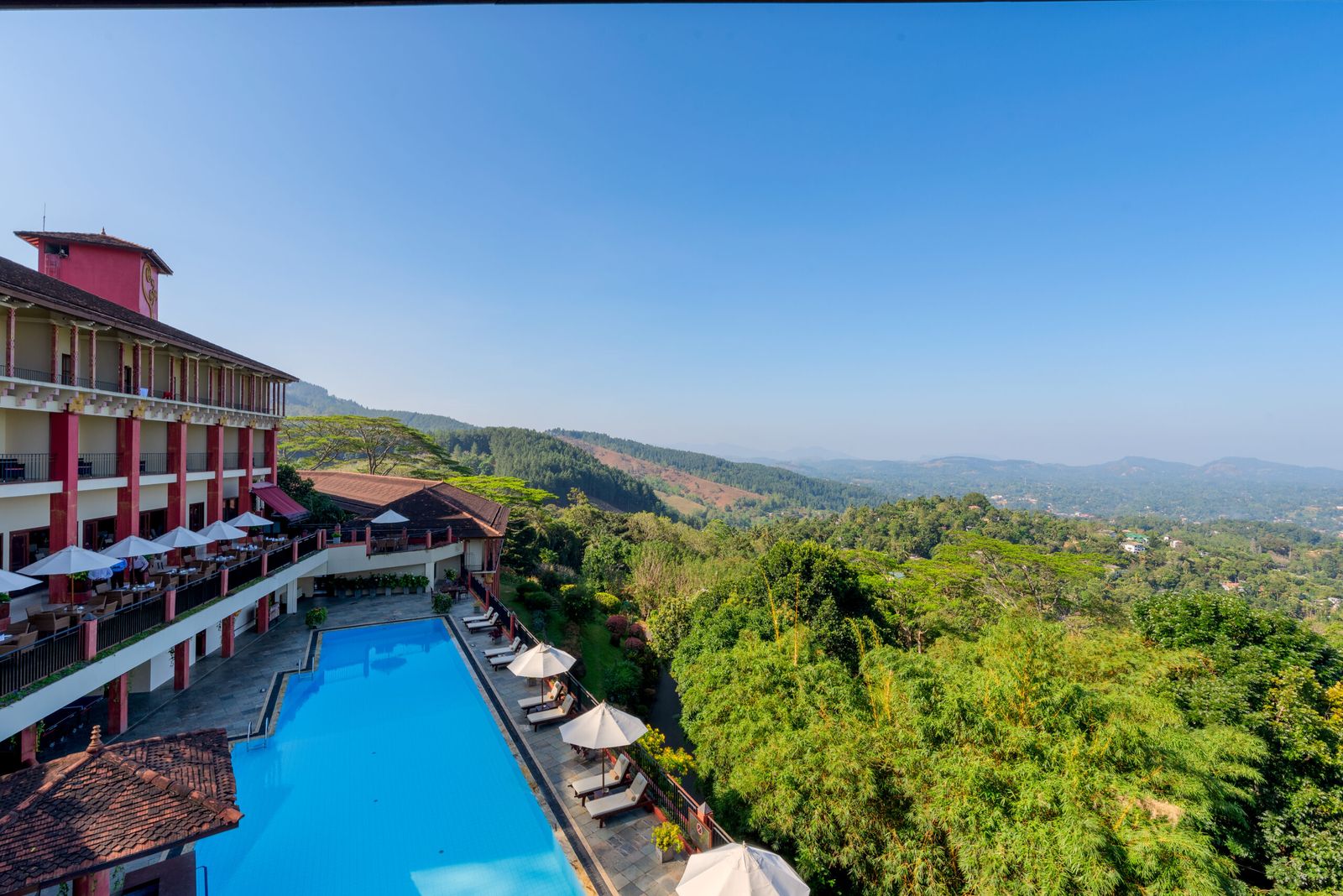 The long pool beside the hotel's balconied wing, looking over forested hills under a blue sky.