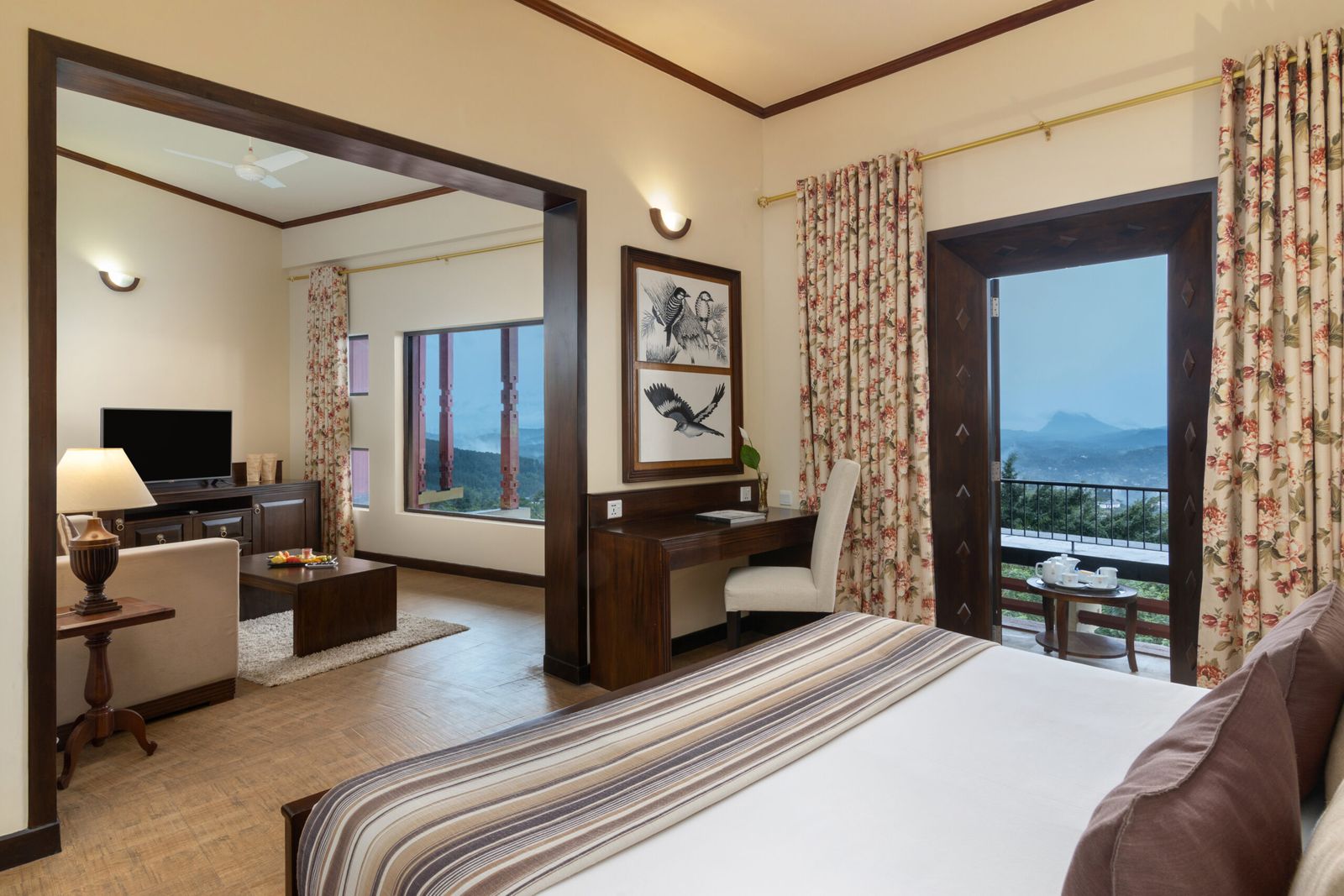 A suite bedroom with a sitting room beyond and a balcony door open to a view of the hills.