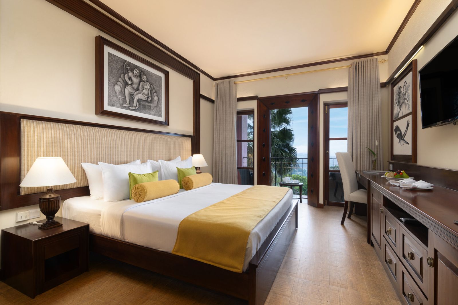 A bedroom with a king bed, a yellow runner, framed drawings and a door to a balcony.