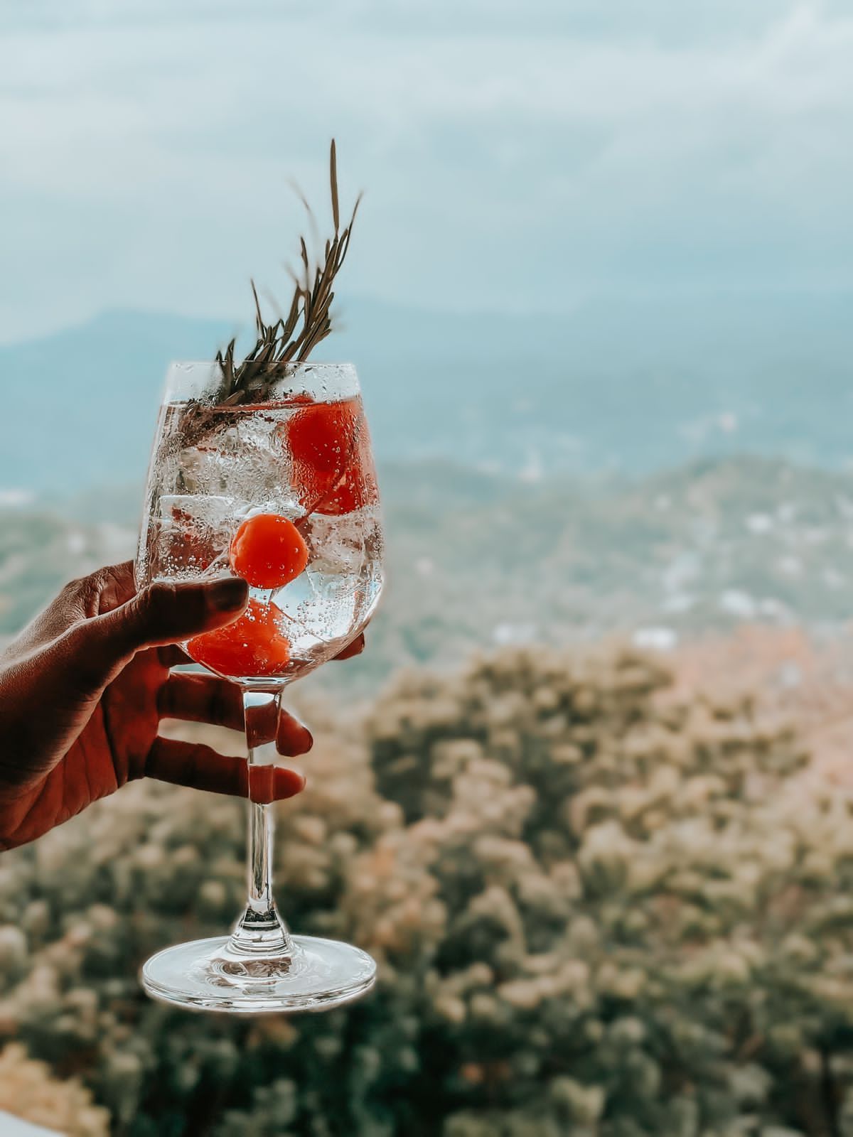 A cocktail held up against a misty hill backdrop