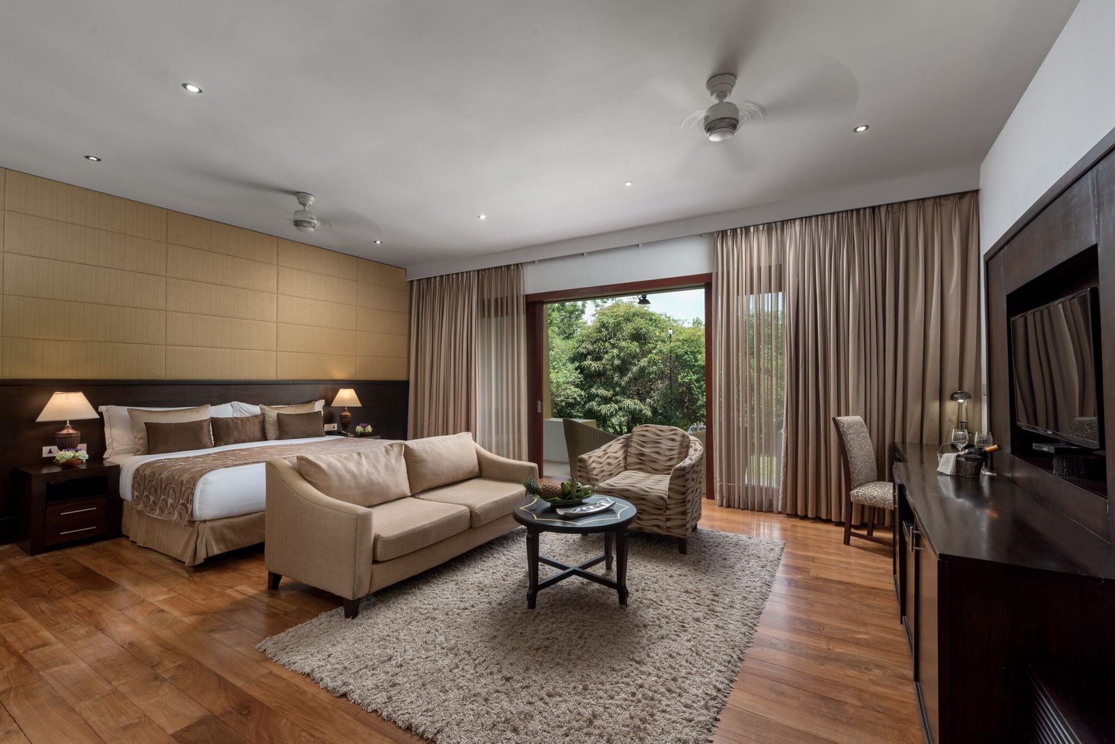 A suite with a bed, a sofa and armchairs on a rug, and glass doors to the garden.