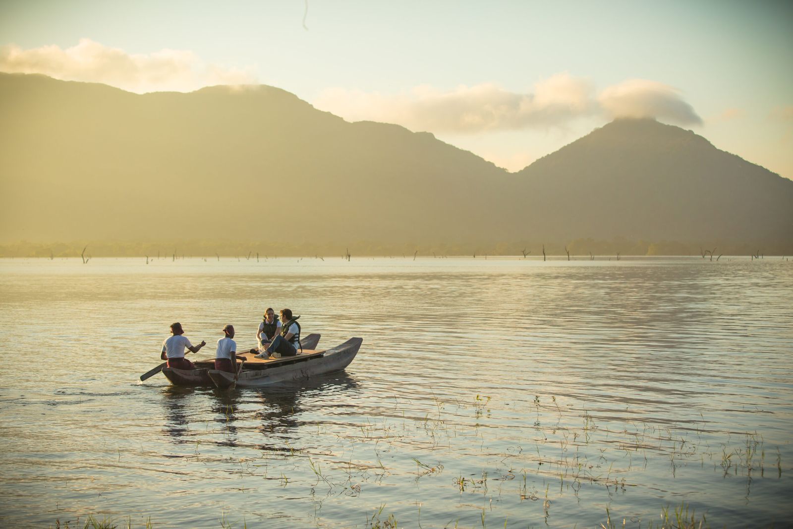 Guests paddling a small boat on Kandalama Lake in hazy light, mountains behind.
