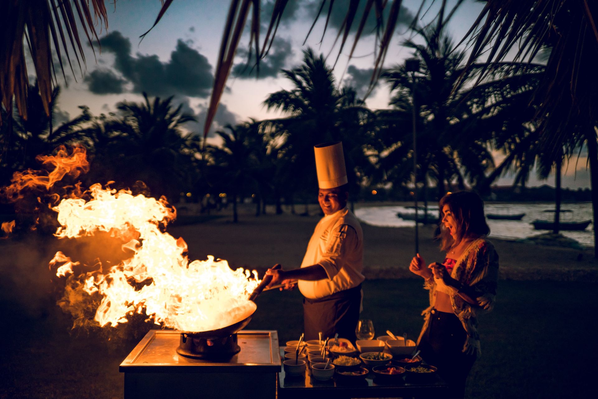 Chef cooking on a wok outdoors as guest looks on