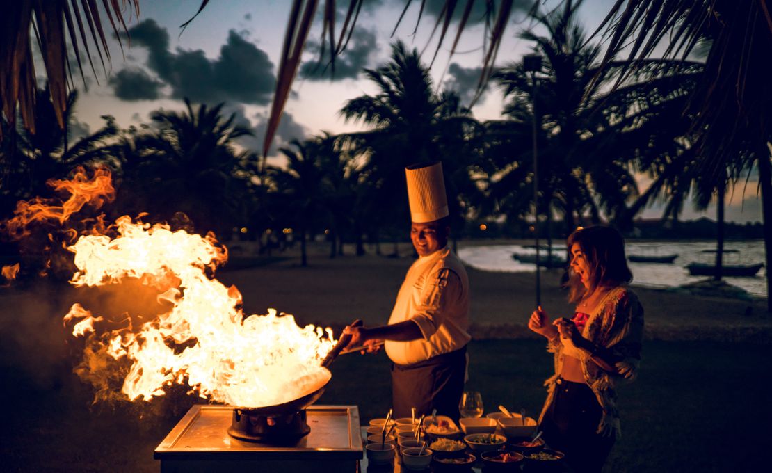 Chef cooking on a wok outdoors as guest looks on